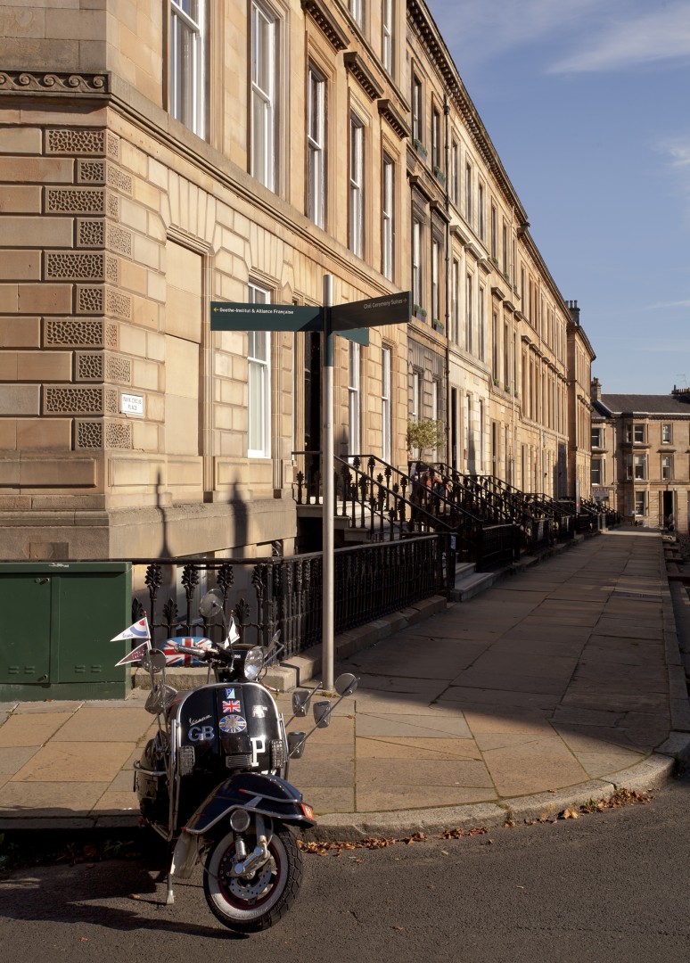 The Unexpected Visitor. Limited edition of 50. Architecture can impose a remarkable sense of order on a city: repeating windows, railings, steps and façades creating rhythms that continue along the street. Here, that carefully ordered perspective is interrupted by something much more ordinary : a scooter parked in the foreground, carrying its own small signs of travel and everyday life. I was drawn to the contrast between the permanence of the buildings and the temporary presence of the scooter. One belongs to the architecture of the city; the other simply happens to be passing through it.