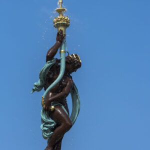 A study in vertical rhythm and classical form. By framing the sculptural figure against an expansive expanse of open sky, this composition isolates the tension between static bronze and the fluid, kinetic energy of falling water. The rich verdigris drapery and deep metallic tones create a timeless anchor, drawing the viewer's eye upward along a clean, architectural axis. Photographer: Stephane Loustalot